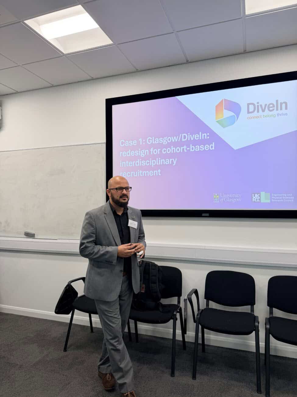 Qammer H. Abbasi presenting to a seminar room, standing beside a screen titled "Case 1: Glasgow/DiveIn: redesign for cohort-based interdisciplinary recruitment," with the DiveIn logo, University of Glasgow crest, and UKRI EPSRC logo displayed.